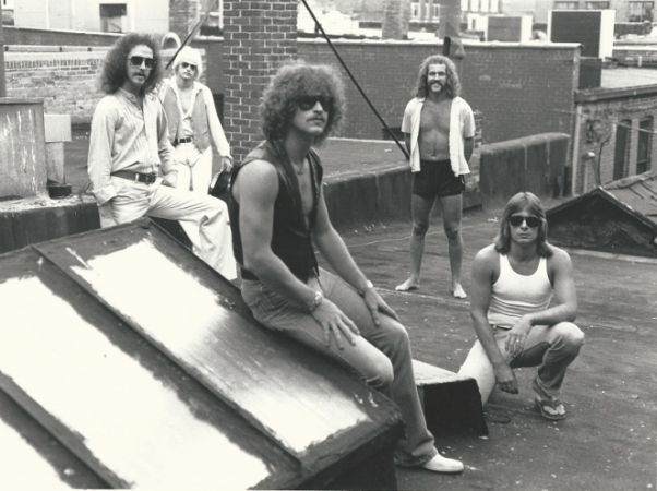 Black and white archival promotional portrait of the rock band At Random posing together on an urban rooftop.